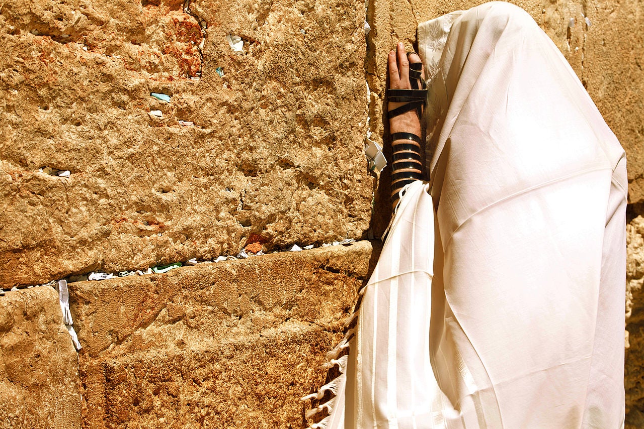 Photo of a man wrapped in a Jewish prayer shawl praying at the Western Wall.