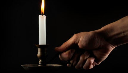Hand holding a lit candle in the dark